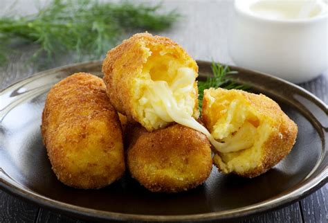 Krokety so syrom a vajíčkom na tanieri s čerstvým paradajkovým šalátom a chladeným nápojom.