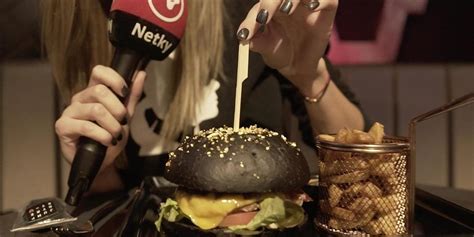 Čierny hamburger posypaný zlatom servírovaný v čiernych rukavičkách